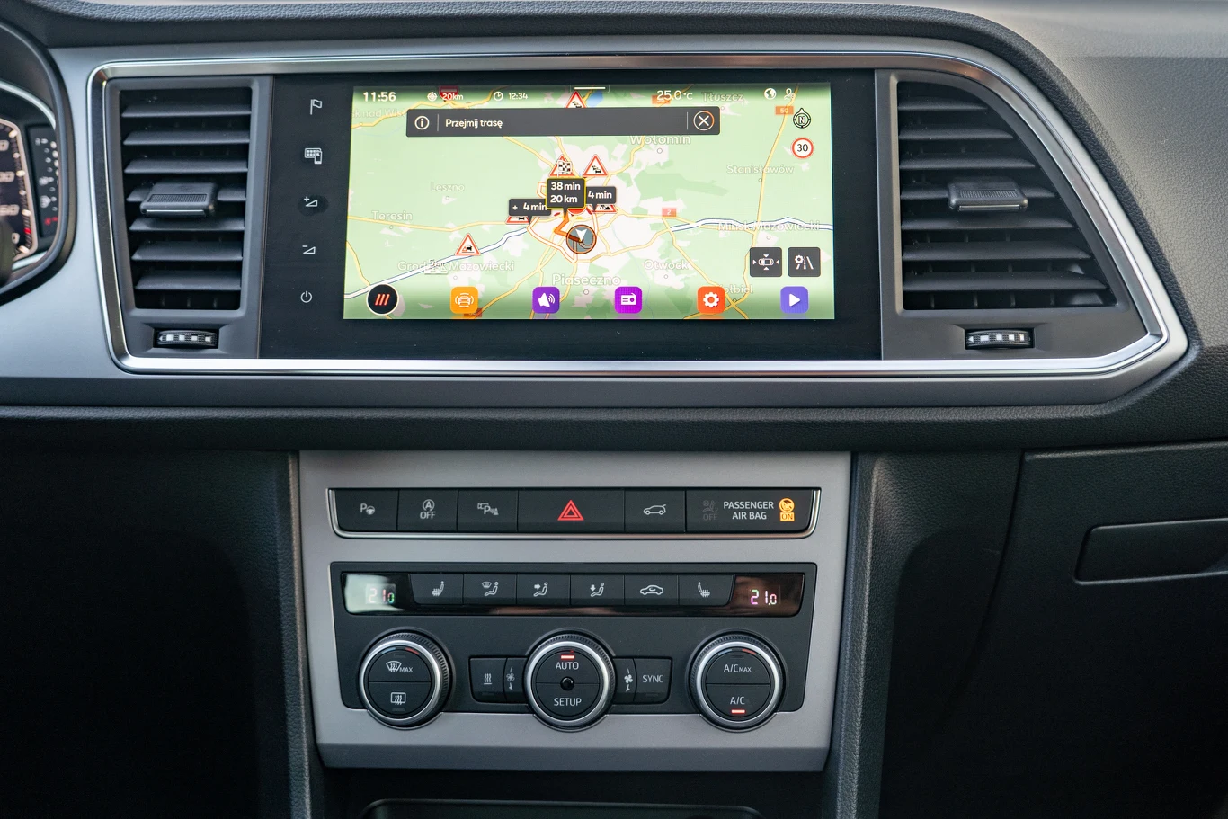 Konsola środkowa samochodu z dużym, kolorowym ekranem nawigacji GPS, poniżej panel sterowania klimatyzacją oraz przyciski do obsługi systemów pojazdu.