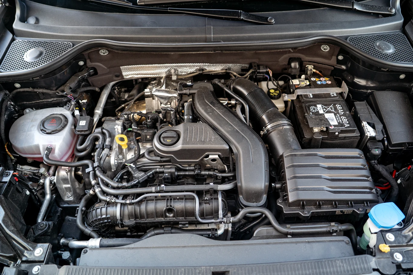 Komora silnika samochodowego z widocznym układem zasilania, akumulatorem po prawej stronie oraz systemem dolotowym powietrza. Wiele przewodów, metalowych i plastikowych elementów mechanicznych oraz zbiornik na płyn chłodniczy po lewej stronie.