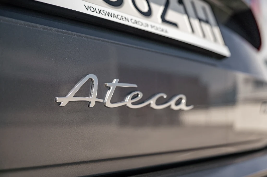 Logo modelu Ateca umieszczone na tylnej klapie samochodu w kolorze ciemnoszarym, w tle widoczny fragment tablicy rejestracyjnej.