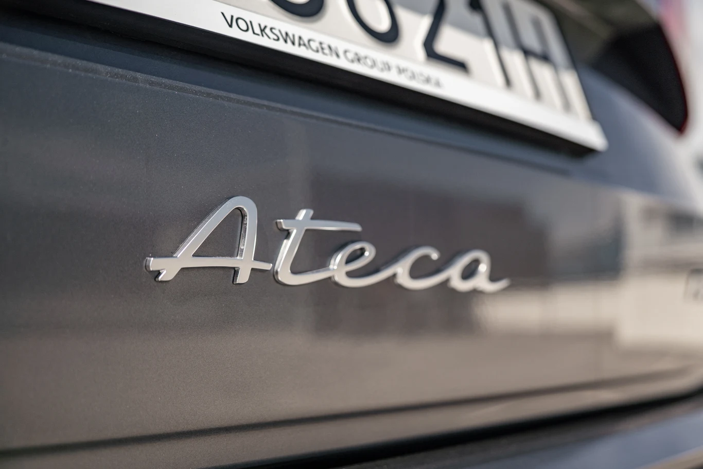 Logo modelu Ateca umieszczone na tylnej klapie samochodu w kolorze ciemnoszarym, w tle widoczny fragment tablicy rejestracyjnej.