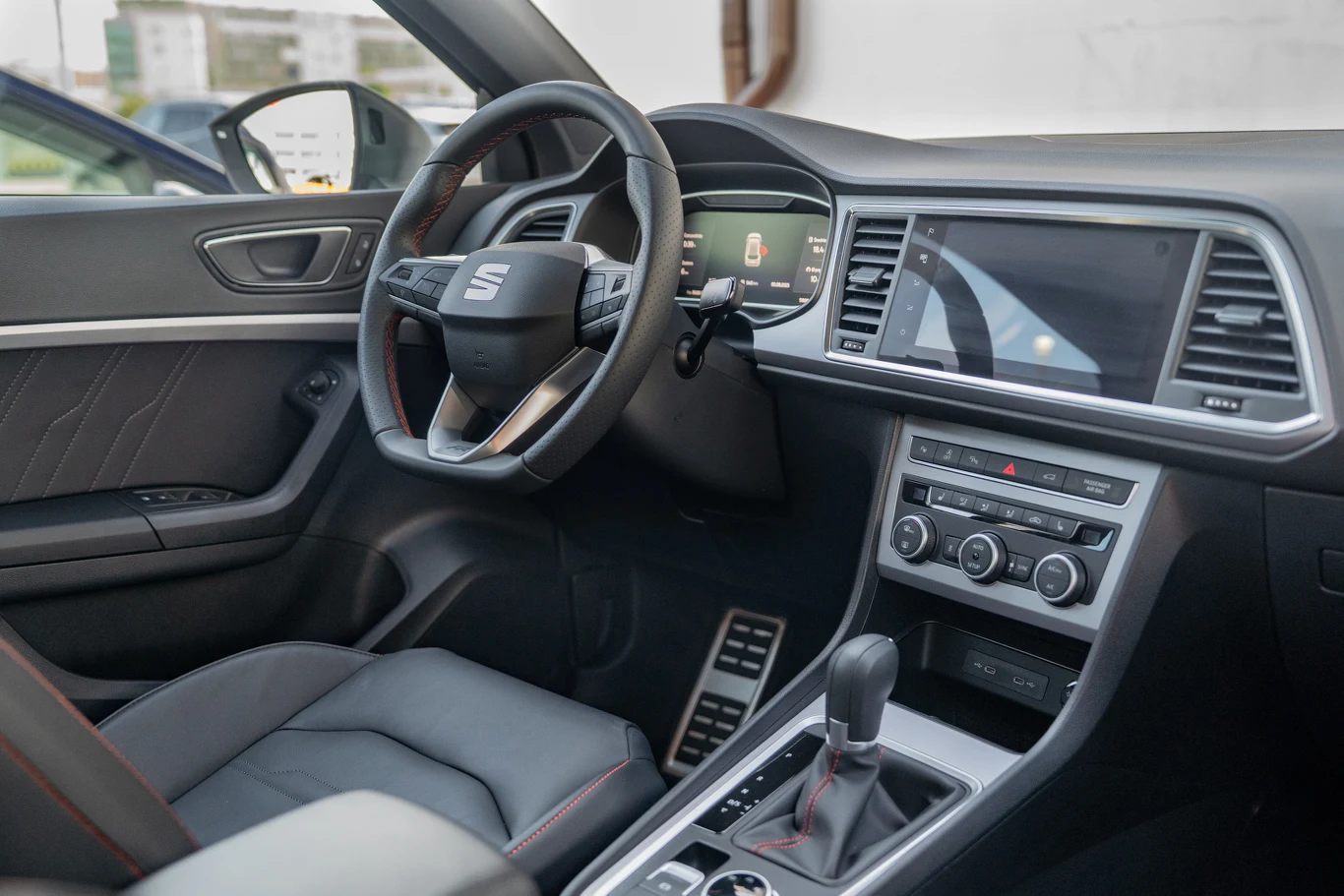 Kokpit nowoczesnego samochodu marki Seat z widoczną kierownicą, deską rozdzielczą, ekranem multimedialnym oraz panelami klimatyzacji i nawiewów. Tapicerka wykonana ze skóry, wnętrze utrzymane w eleganckim, czarnym kolorze.