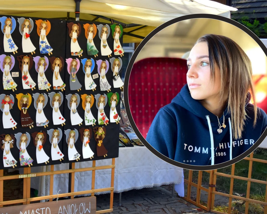 Anioły z Lanckorony i Anna Twardosz (w ramce) Stoisko wystawowe z ręcznie wykonanymi aniołkami z różnych materiałów, ułożonymi w kilku rzędach na czarnych tablicach. W prawym górnym rogu znajduje się okrągła ramka z portretem młodej kobiety w bluzie Tommy Hilfiger, która patrzy w bok. W tle widać ...