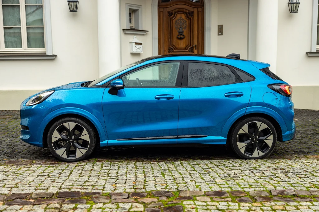 Samochód wyjeżdża z salonu na obręczach o średnicy 17 lub 18 cali Nowoczesny niebieski samochód zaparkowany na brukowanym podjeździe przed eleganckim budynkiem z drewnianymi drzwiami i białymi kolumnami.