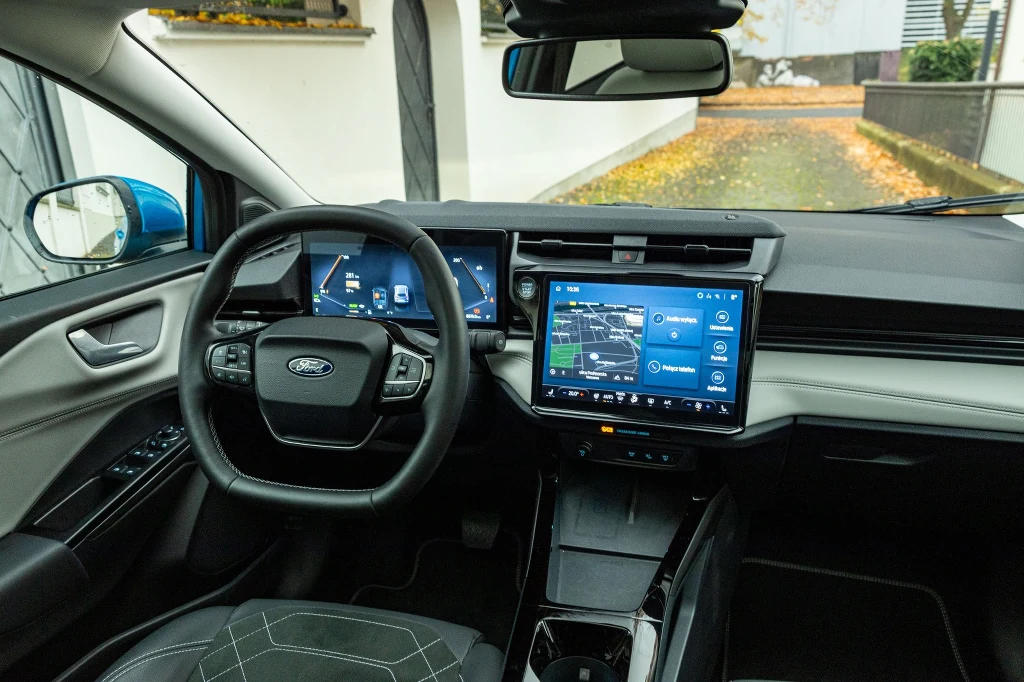 Dźwignia wyboru kierunku jazdy z tunelu środkowego trafiła za kierownicę Nowoczesna deska rozdzielcza samochodu Ford z cyfrowym panelem wskaźników, dużym ekranem dotykowym na konsoli centralnej oraz skórzaną kierownicą, całość utrzymana w czarnej kolorystyce.