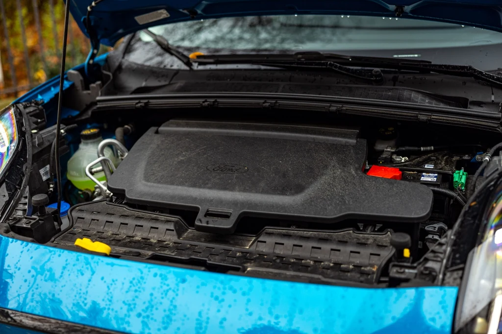 Przedni bagażnik ma 43 litry i jest schowany pod dodatkową klapką Otwarta maska niebieskiego samochodu z widocznym silnikiem i elementami komory silnika, takimi jak akumulator oraz przewody.