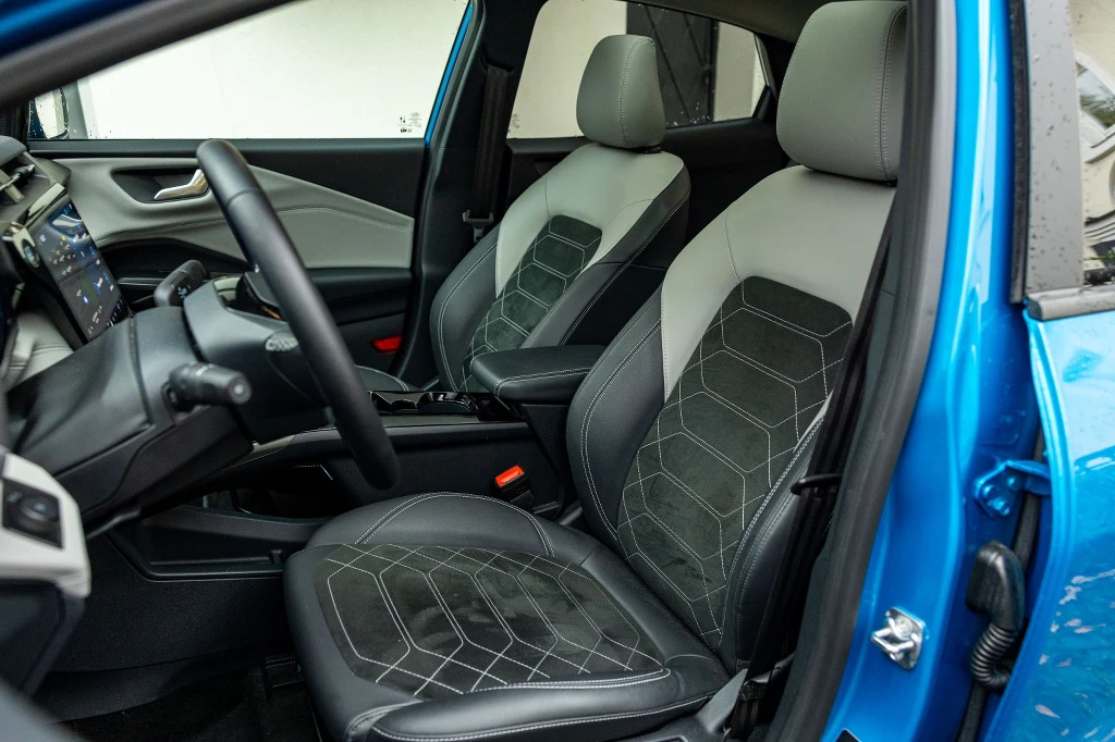 Sztuczna skóra i elementy z materiału przypominającego alkantarę – to elementy wyposażenia wersji Premium Wnętrze nowoczesnego samochodu z widocznym miejscem kierowcy i pasażera, czyste, zadbane fotele w czarno-szarej kolorystyce oraz wyraźnie widoczny kokpit z panelem sterowania.