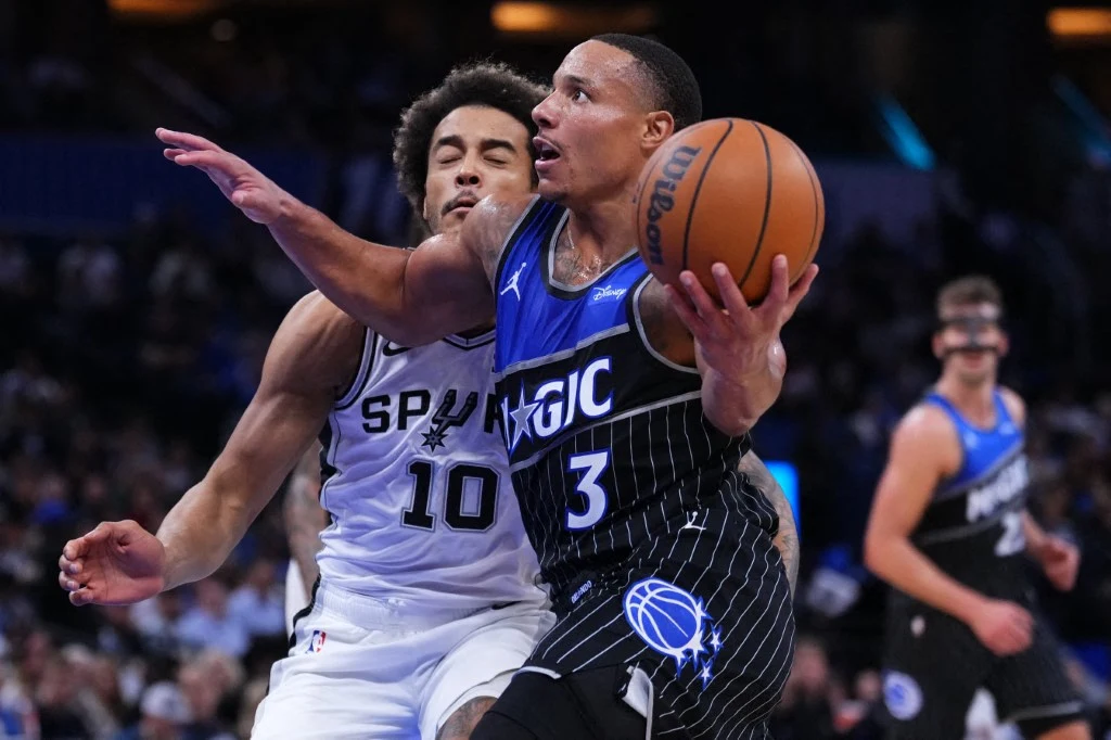 Jeremy Sochan ma za sobą kolejny mecz w NBA Dwóch koszykarzy rywalizuje podczas dynamicznego wejścia pod kosz, jeden z zawodników w czarnej koszulce z numerem 3 trzyma piłkę i próbuje oddać rzut, zawodnik w białej koszulce próbuje go zablokować.