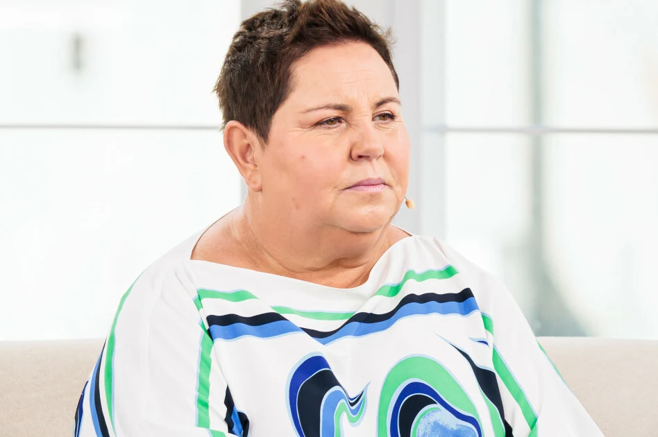 Dorota Wellman Dorota Wellman w jasnym wnętrzu, krótko ostrzyżona, w kolorowej bluzce, z mikrofonem przy twarzy.