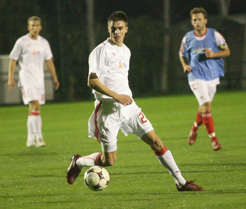 Michał Zieliński w reprezentacji Polski zagrał tylko raz Piłkarz w białym stroju wykonuje dynamiczne podanie piłki podczas meczu wieczorową porą, w tle kilku innych zawodników na boisku.