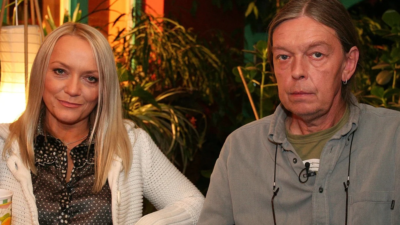 Małgorzata Ostrowska i Jacek Gulczyński w 2006 r. podczas nagrania programu "Zacisze gwiazd" Dwie osoby siedzące obok siebie, kobieta z długimi blond włosami uśmiecha się delikatnie, mężczyzna o długich włosach patrzy poważnie w stronę aparatu, w tle bujna zieleń roślin doniczkowych i ciepłe światło lampy.