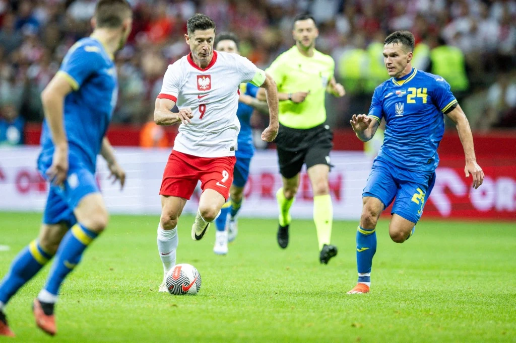 Ukraina i Polska mogą zagrać przeciwko sobie w finale baraży o mundial 2026 Piłkarze reprezentacji Polski i Ukrainy rywalizujący w trakcie meczu piłki nożnej, zawodnik w biało-czerwonym stroju prowadzi piłkę atakowany przez zawodników w niebieskich strojach, w tle widoczni kibice.