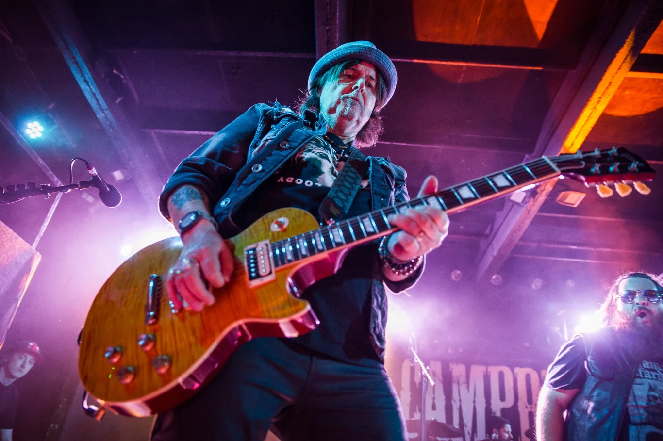 Phil Campbell powróci do Polski Gitarzysta w kapeluszu gra na gitarze elektrycznej na scenie podczas koncertu rockowego, w tle efekty świetlne i inni członkowie zespołu.
