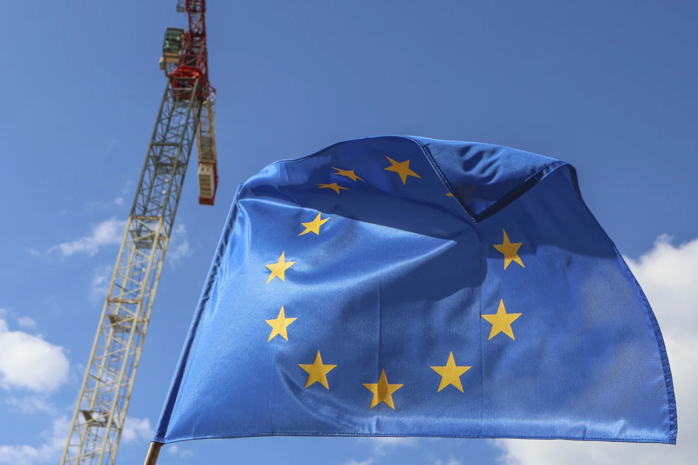 Państwa UE przyjęły klauzulę ochronną ws. Mercosur. Powiewająca flaga Unii Europejskiej na pierwszym planie na tle nieba z widocznym żurawiem budowlanym w tle.