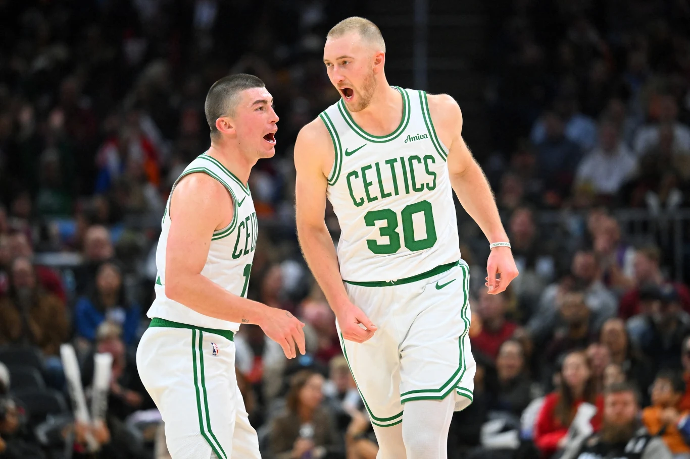 Dwóch koszykarzy drużyny Boston Celtics na parkiecie w trakcie meczu, obaj w białych strojach z zielonymi napisami, jeden z nich energicznie pokazuje emocje, drugi jest w ruchu, w tle rozmyta publiczność.