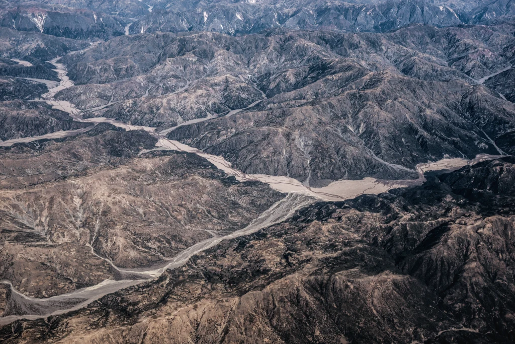 Rozległy, suchy krajobraz górski poprzecinany wijącymi się korytami rzek i strumieni, z wyraźnie zaznaczonymi pasmami górskimi oraz spękaną, skalistą powierzchnią.
