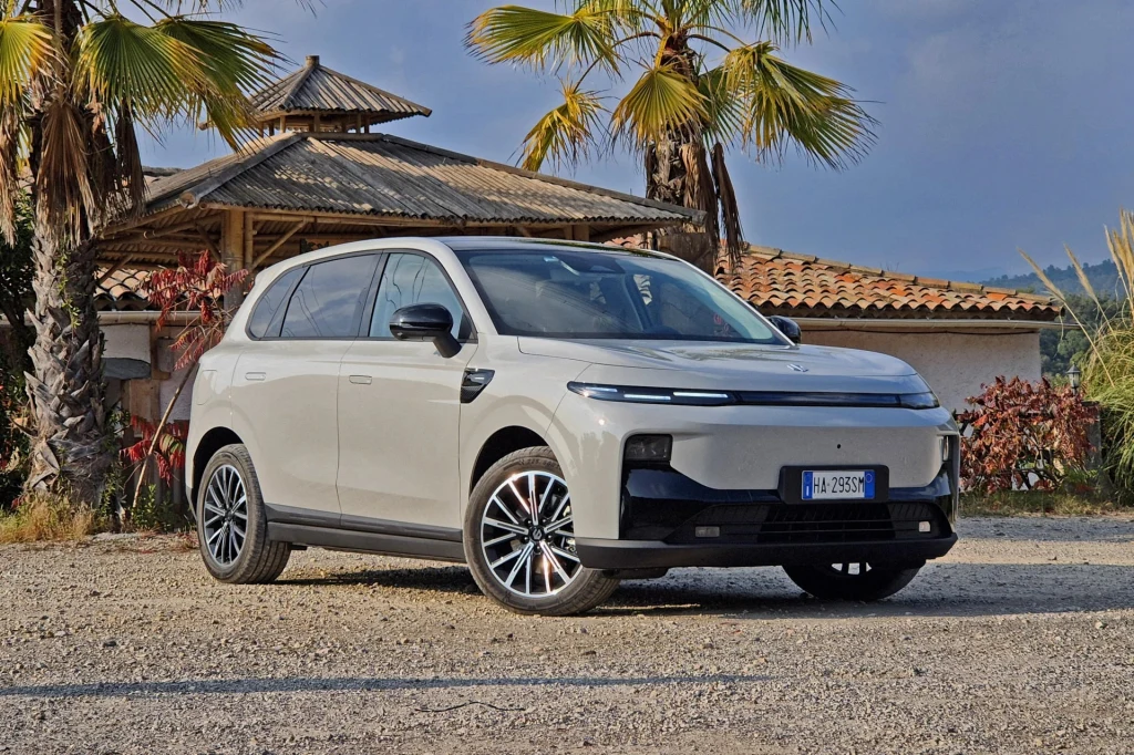 Leapmotor B10 to, zdaniem chińskich ekspertów, jeden z najlepszych tamtejszych samochodów elektrycznych. Jasnoszary SUV nowoczesnej konstrukcji zaparkowany na żwirowym podjeździe, w tle egzotyczne palmy oraz budynek o drewnianym dachu. Słoneczne światło podkreśla linię nadwozia samochodu.