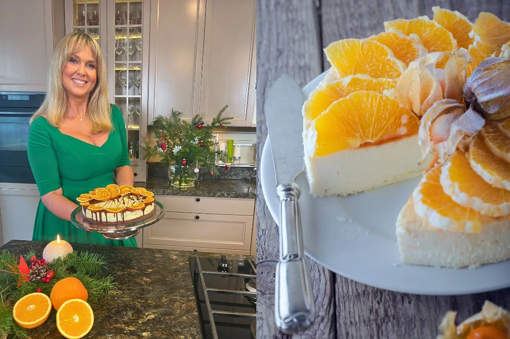 Ewa Wachowicz poleca przepisy na świąteczne serniki Uśmiechnięta kobieta w zielonej sukience prezentuje sernik ozdobiony plasterkami pomarańczy i czekolady, na drugim planie zbliżenie na kawałek tego samego deseru z efektowną dekoracją z owoców i ciasta, w tle świąteczna dekoracja i przekrojone pomarańcze.