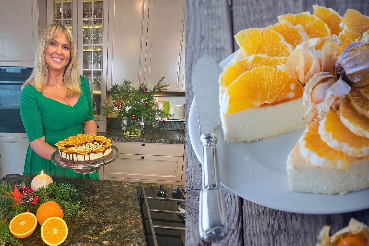 Ewa Wachowicz poleca przepisy na świąteczne serniki Uśmiechnięta kobieta w zielonej sukience prezentuje sernik ozdobiony plasterkami pomarańczy i czekolady, na drugim planie zbliżenie na kawałek tego samego deseru z efektowną dekoracją z owoców i ciasta, w tle świąteczna dekoracja i przekrojone pomarańcze.