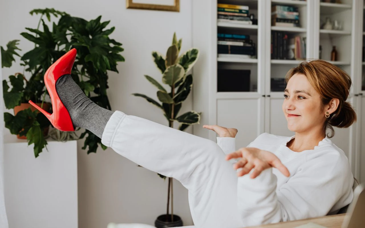 Sportowe ubranie zostaw w domu. To tylko jeden wieczór w roku, niech dobrze to zapamiętają Kobieta siedząca w jasnym pomieszczeniu, ubrana na biało, z wysuniętą nogą w czerwonym, wysokim obcasie i szarej skarpetce, z gestem rozłożonych rąk, w tle rośliny doniczkowe i regał z książkami.