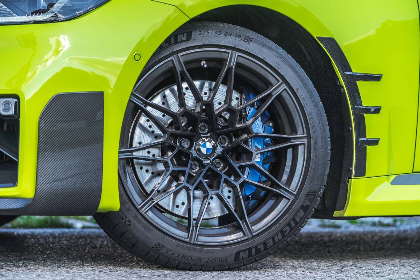 BMW M2 ma taki sam rozmiar felg jak M4, ale nie dostaniemy tu ceramicznych hamulców Detal felgi aluminiowej z logo BMW oraz sportowego zacisku hamulcowego na tle jasnożółtego nadwozia samochodu sportowego.