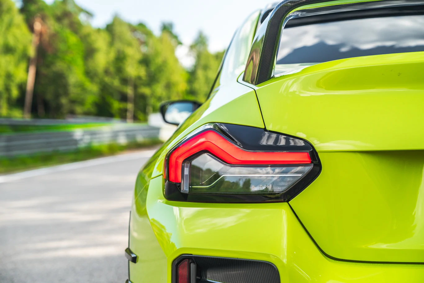 BMW M2 Jaskrawozielony tył sportowego samochodu z nowoczesną lampą tylną na tle asfaltowej drogi i zielonego lasu.