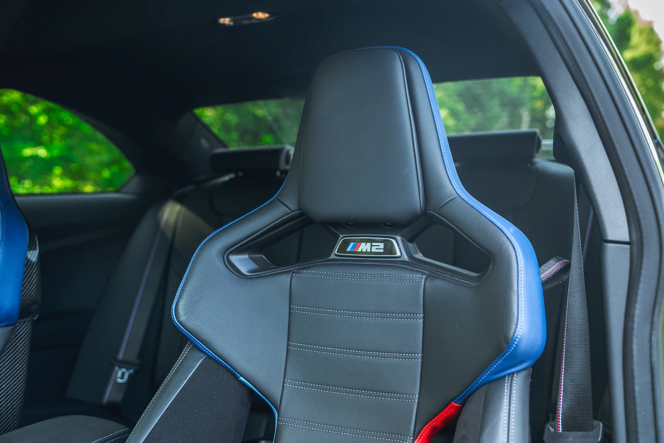 BMW M2 Sportowy fotel samochodowy z logo M2, obszyty czarną skórą z niebieskimi akcentami, na tle wnętrza nowoczesnego pojazdu.