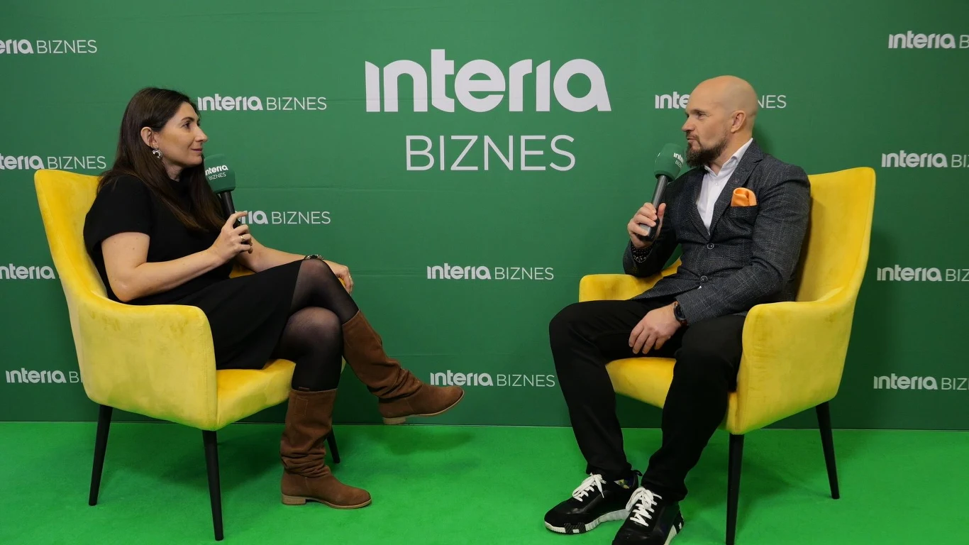 Grupa Unilink myśli o dalszej ekspansji Dwie osoby siedzą na żółtych fotelach na tle zielonej ściany z logotypami interia BIZNES, rozmawiają ze sobą trzymając mikrofony.