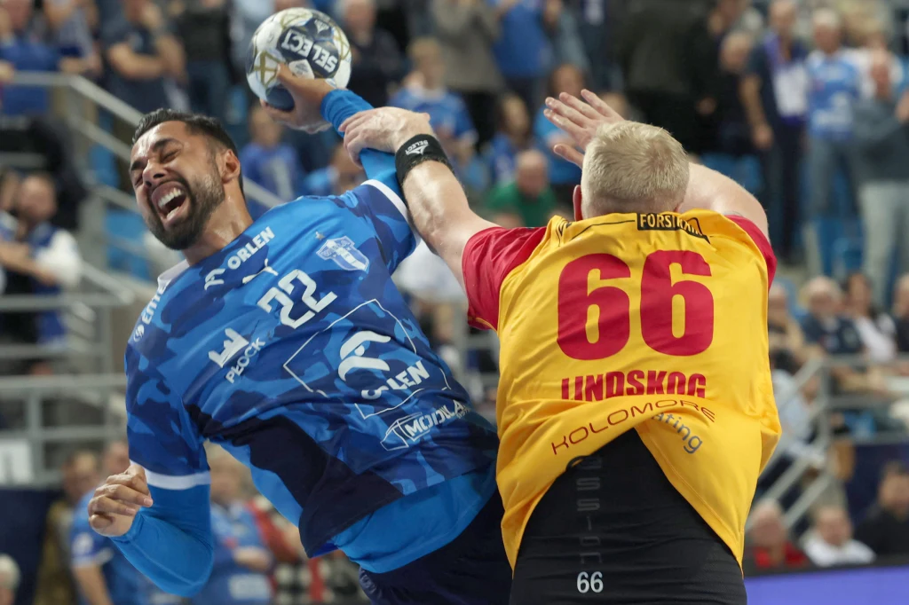 Moment dynamicznej walki podczas meczu piłki ręcznej, dwóch zawodników ściera się w kontakcie fizycznym, zawodnik w niebieskiej koszulce numer 22 trzyma piłkę, a rywal w żółto-czerwonej koszulce z numerem 66 blokuje jego ruch.