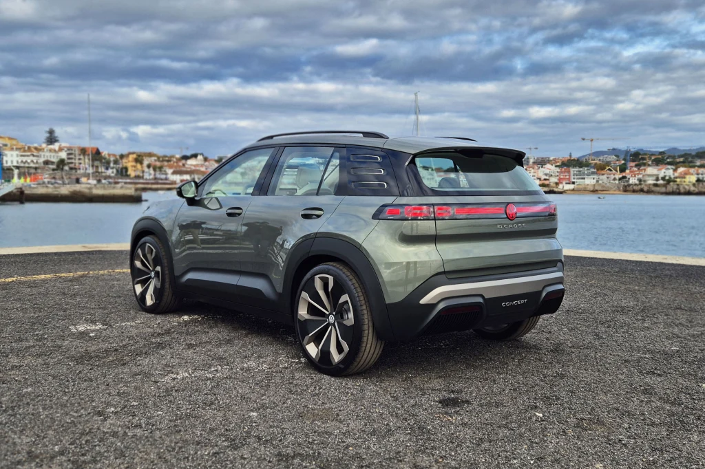 Nowoczesny, zielony samochód terenowy SUV zaparkowany na asfaltowej nawierzchni z widokiem na wodę i zabudowania miejskie w tle. Auto wyróżnia się stylowymi felgami, opływową sylwetką i nowoczesnymi detalami.