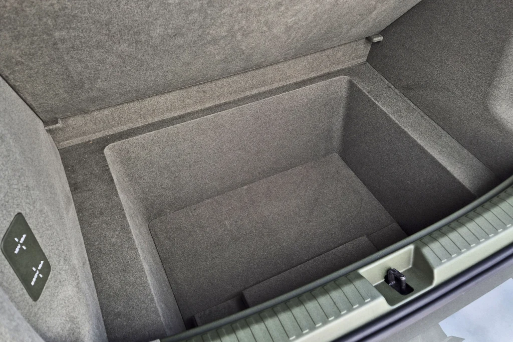 Wnętrze bagażnika samochodu z dodatkową, głęboką wnęką na przedmioty, wykończone szarym materiałem tapicerowanym.