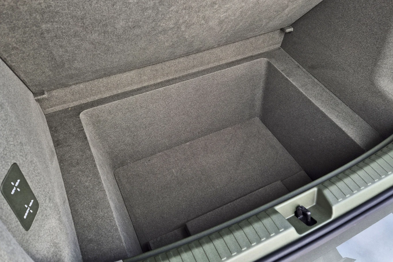 Wnętrze bagażnika samochodu z dodatkową, głęboką wnęką na przedmioty, wykończone szarym materiałem tapicerowanym.
