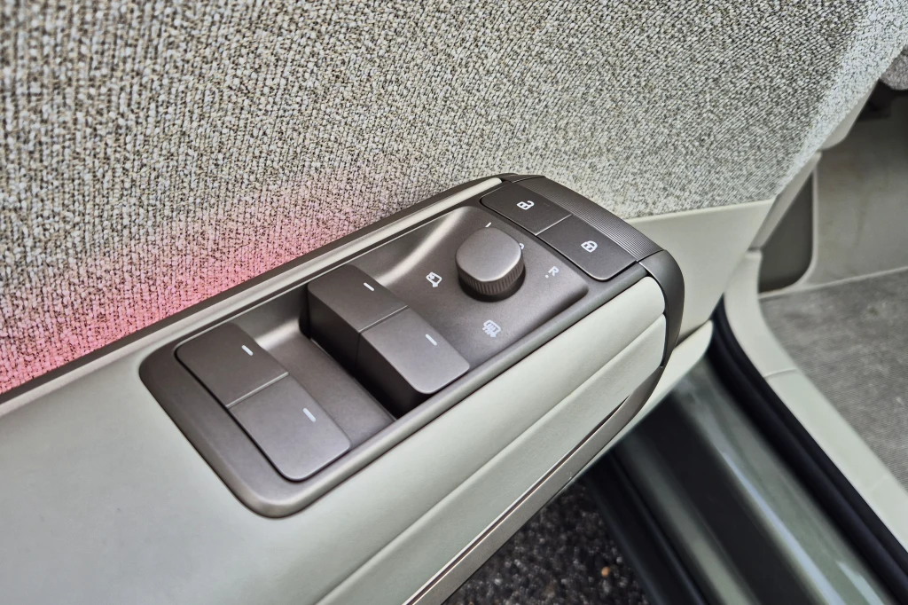 Panel sterowania szybami i lusterkami bocznymi zamontowany w drzwiach samochodu, z widocznymi przyciskami i pokrętłem na tle tapicerki wewnętrznej.