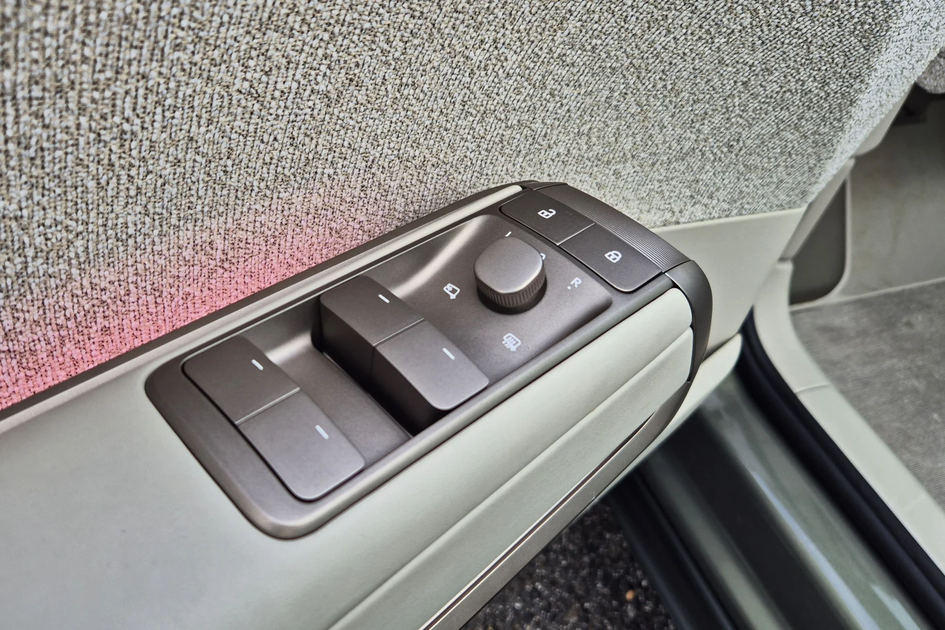 Panel sterowania szybami i lusterkami bocznymi zamontowany w drzwiach samochodu, z widocznymi przyciskami i pokrętłem na tle tapicerki wewnętrznej.