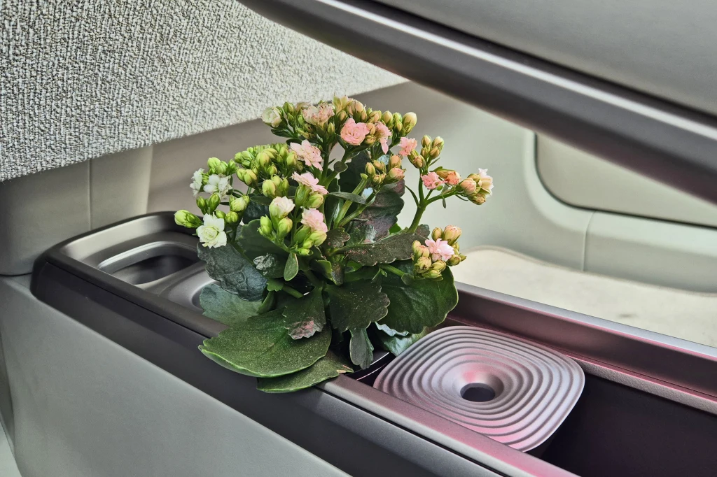 Doniczka z zieloną rośliną kwitnącą na różowo umieszczona we wnęce samochodowego wnętrza z metaliczną ozdobą obok.