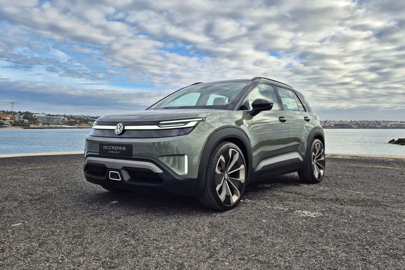 Nowoczesny SUV marki Volkswagen zaparkowany na tle wody i panoramy miasta, pod pochmurnym niebem. Samochód wyróżnia się dużymi felgami, aerodynamiczną sylwetką oraz stylowymi reflektorami LED.