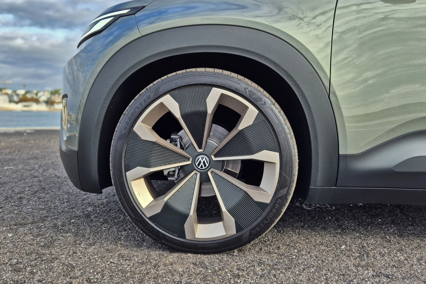Duże aluminiowe felgi o nowoczesnym wzorze na tle asfaltowej nawierzchni, widoczny fragment nadkola oraz błotnika samochodu Volkswagen w odcieniach szarości.