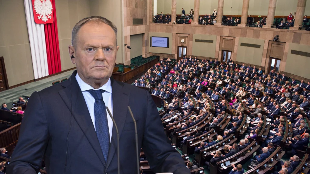 Premier wygłaszający przemówienie na tle sali plenarnej polskiego Sejmu z widocznymi posłami oraz dużą flagą biało-czerwoną z godłem państwowym.