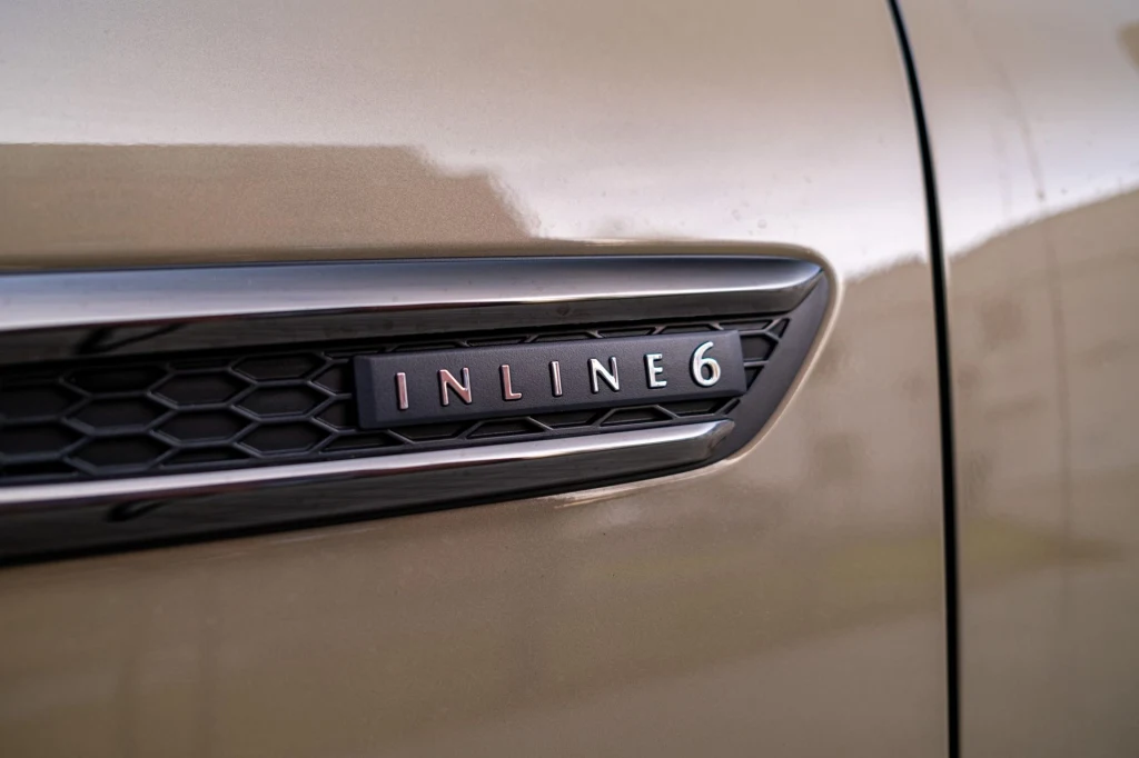 Emblemat z napisem INLINE 6 umieszczony na karoserii samochodu, widoczny fragment wentylacyjnego wlotu powietrza i metaliczny lakier pojazdu.