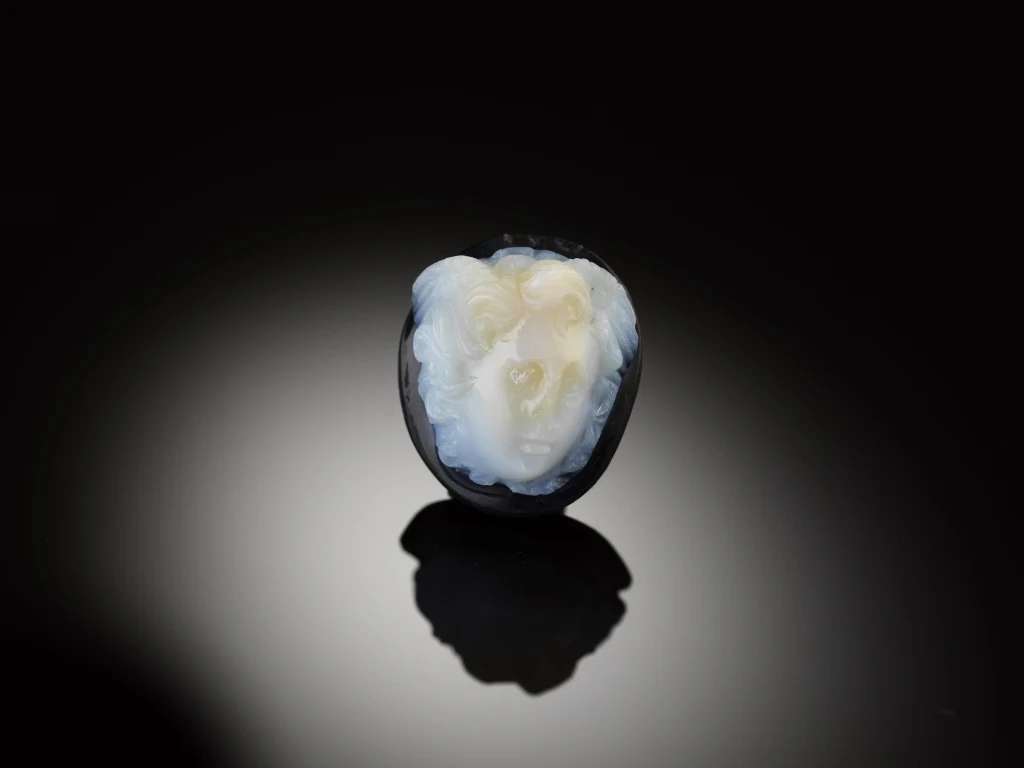 Winogrono przekrojone na pół, w którego wnętrzu jasny miąższ układa się w kształt przypominający ludzką twarz, całość sfotografowana na ciemnym tle.