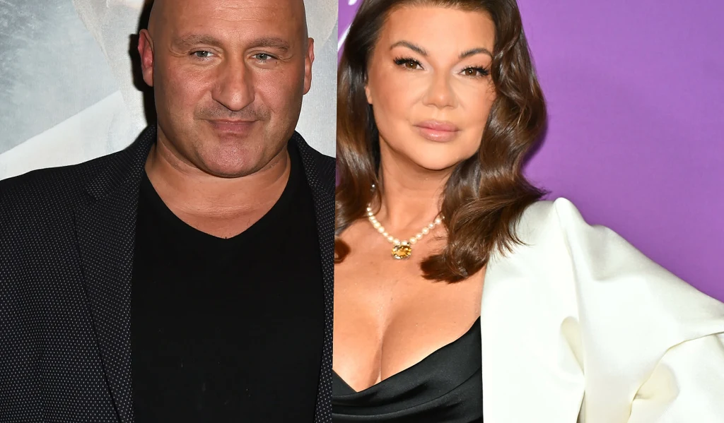 Marcin Najman i Edyta Górniak Dwoje dorosłych ludzi w eleganckich strojach na tle ozdobnej ściany, mężczyzna w ciemnej marynarce oraz kobieta w białym żakiecie z perłowym naszyjnikiem, oboje z poważnymi wyrazami twarzy.