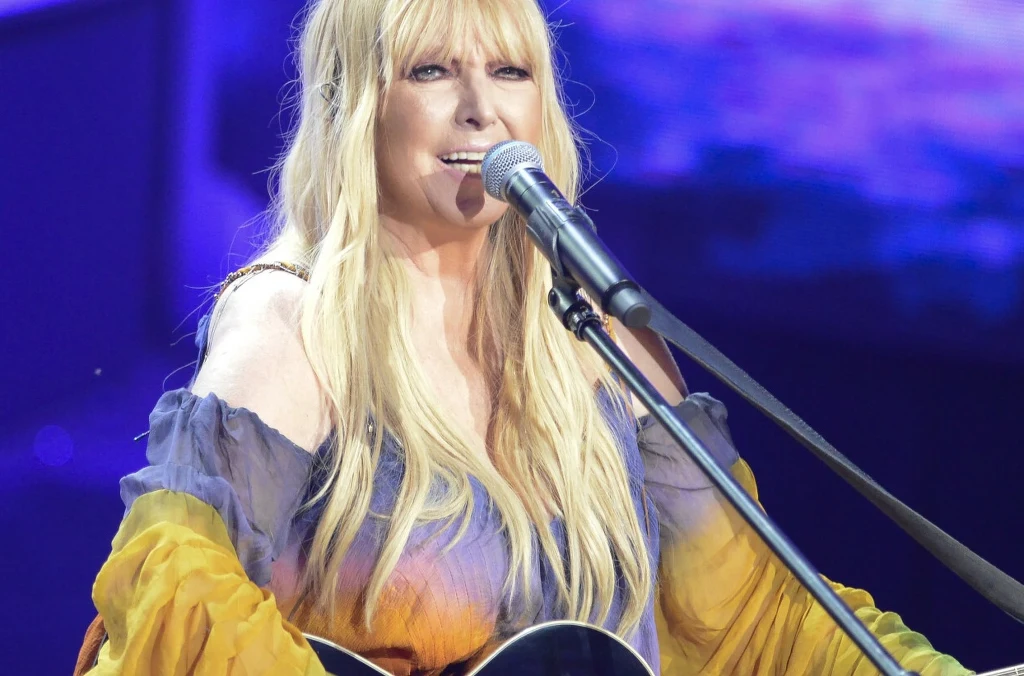 Wykonanie Maryli Rodowicz "Jadą wozy kolorowe" zdobyło serca widzów Kobieta z długimi, blond włosami śpiewa do mikrofonu na scenie, trzymając gitarę. Ubrana w kolorową, zwiewną sukienkę, oświetlona przez sceniczne światła, na tle fioletowo-niebieskiego tła.