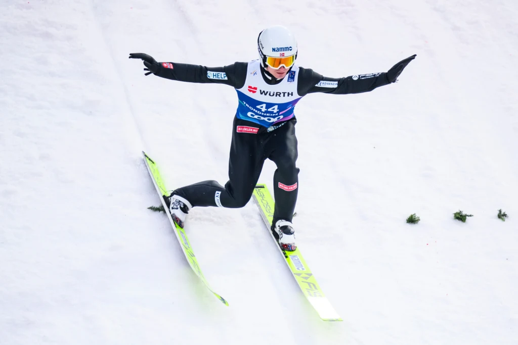 Kristoffer Eriksen Sundal wycofał się z jednego z konkursów z powodu awarii kombinezonu Skoczek narciarski lądujący na śniegu w trakcie zawodów, ubran w profesjonalny kombinezon i kask, z rozpostartymi ramionami dla utrzymania równowagi.