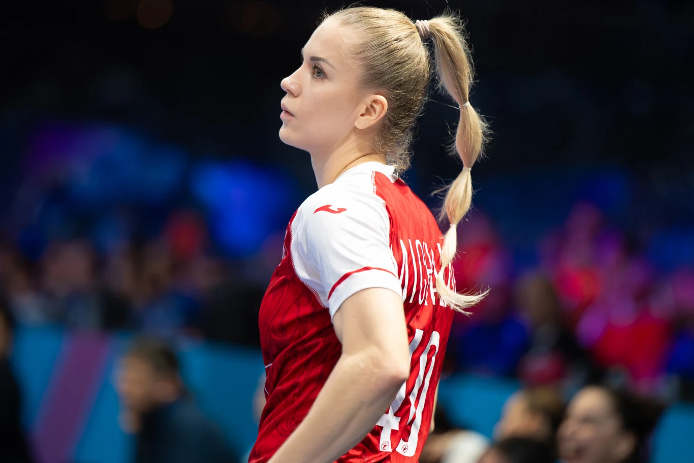 Daria Michalak przyznaje, że w starciu z Holandią Polki chcą walczyć o swoje marzenia Sportowczyni w czerwono-białym stroju drużynowym obserwuje boisko, jej długie blond włosy zostały spięte w wysoki kucyk. W tle rozmyte sylwetki kibiców i innych zawodniczek, dominują niebieskie i czerwone kolory.