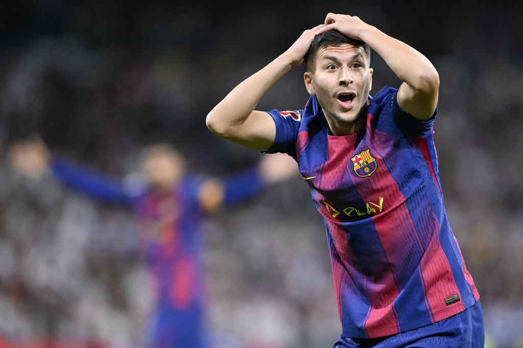Piłkarz w stroju FC Barcelony z rękami na głowie wyraża silne emocje podczas meczu, a w rozmytym tle widoczny jest inny zawodnik na boisku.