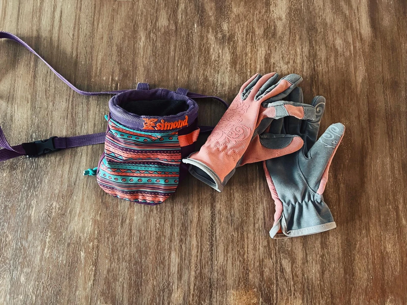 Torba na magnezję w wielokolorowe wzory oraz para sportowych rękawiczek leżących na drewnianej powierzchni.