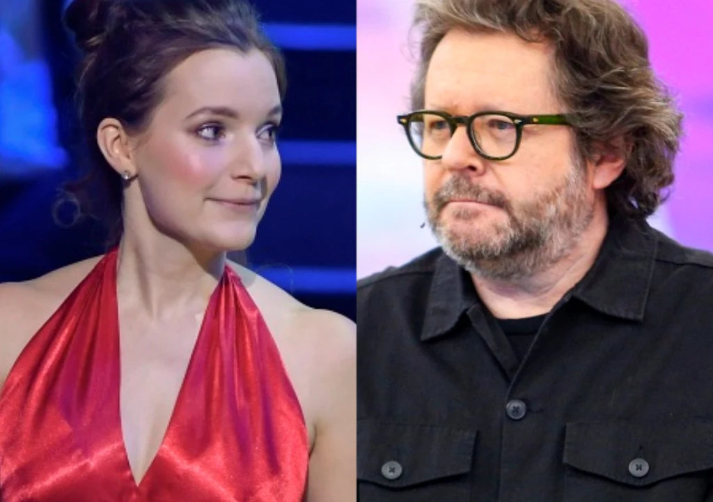 Po lewej stronie kobieta w eleganckiej, czerwonej sukni z upiętymi włosami, po prawej stronie mężczyzna w okularach i czarnej koszuli z zarostem, oboje na tle scenicznego oświetlenia.