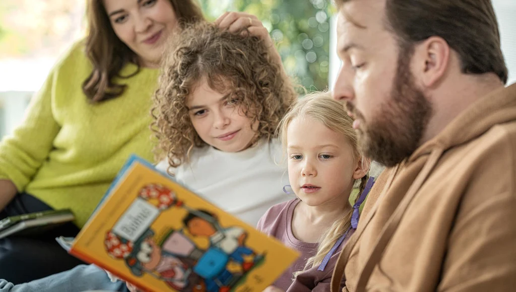 Często rozpoczęcie trudnego tematu jest łatwiejsze, gdy zaczyna się od książki Rodzina spędza wspólnie czas na kanapie, dorosły mężczyzna czyta książkę dwójce dzieci, podczas gdy kobieta z uśmiechem towarzyszy im z boku. Książka ma kolorową okładkę z ilustracjami.