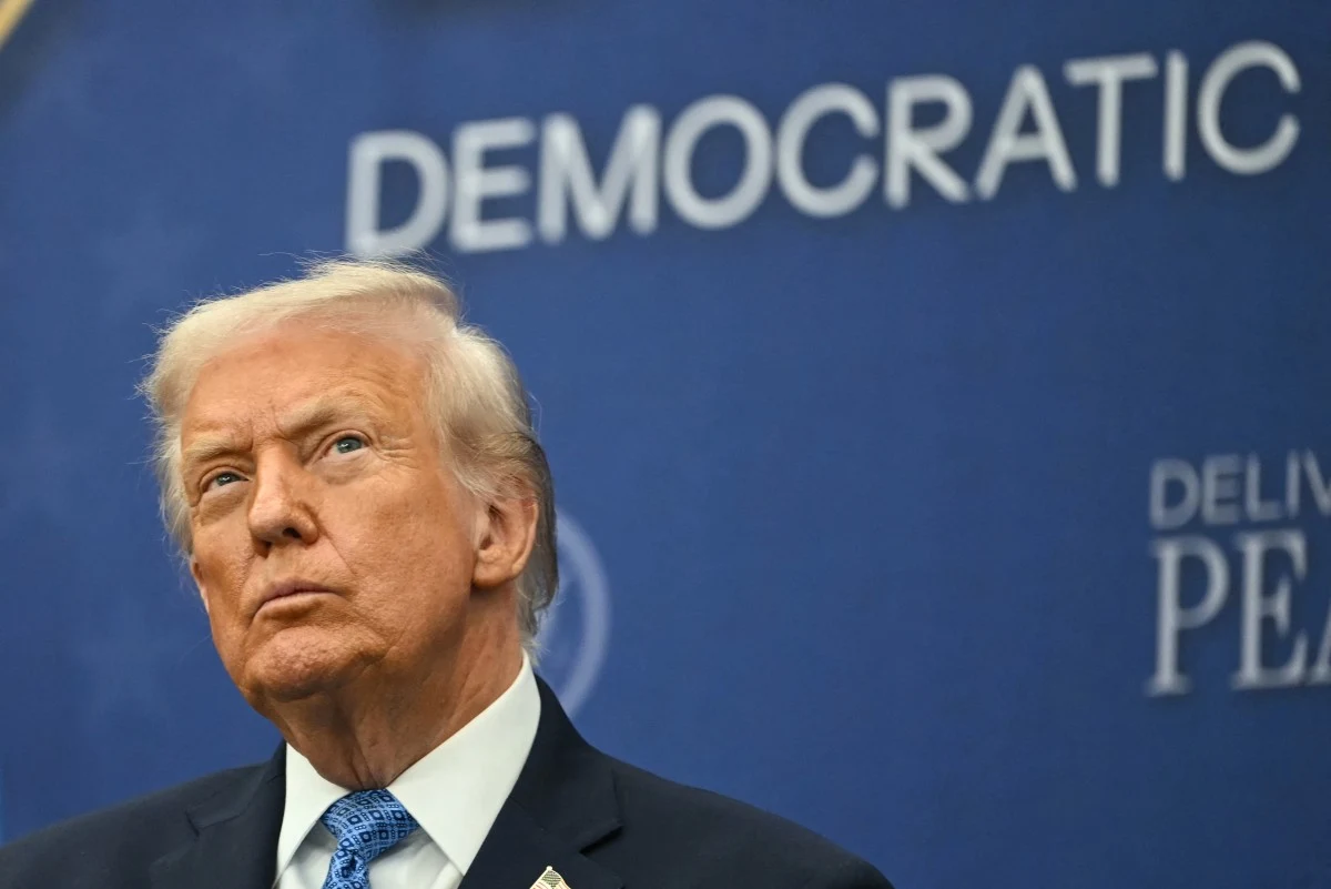 Donald Trump ma plan na pokój na Bliskim Wschodzie Mężczyzna w garniturze z poważnym wyrazem twarzy stoi na tle niebieskiego baneru z widocznym napisem 'DEMOCRATIC'.