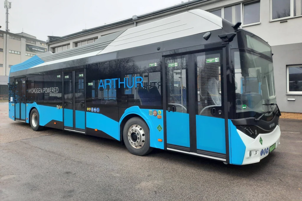 Nowoczesny autobus o napędzie wodorowym w kolorze niebiesko-czarnym stoi zaparkowany na tle przemysłowych budynków. Na nadwoziu widoczne oznaczenia dotyczące zasilania wodorem oraz napis ARTHUR.