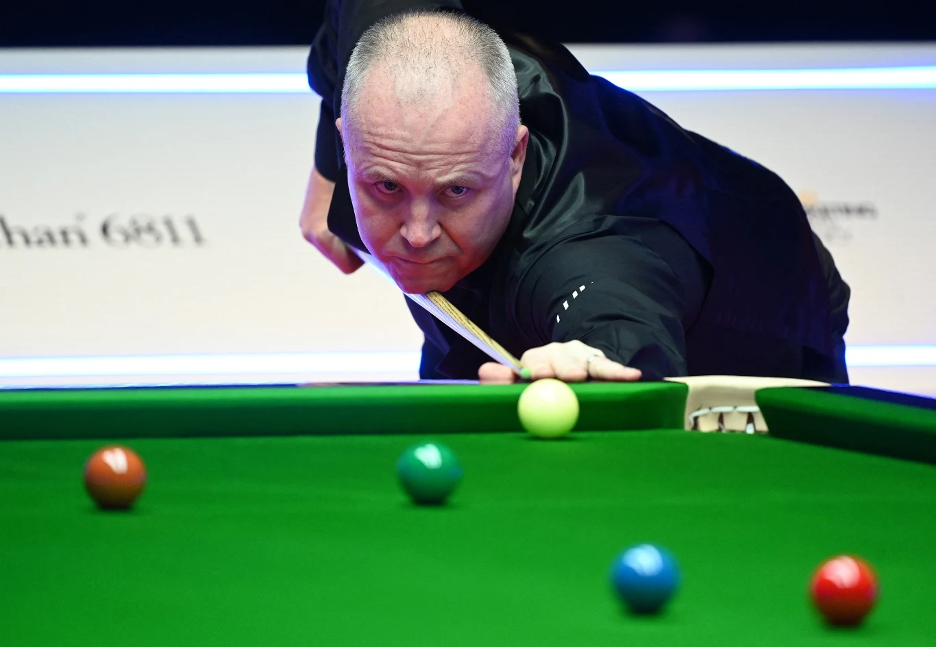 John Higgins Zawodnik skupiony na wykonaniu precyzyjnego zagrania przy stole bilardowym, widoczne kolorowe bile rozłożone na zielonym suknie, światło skoncentrowane na akcji.
